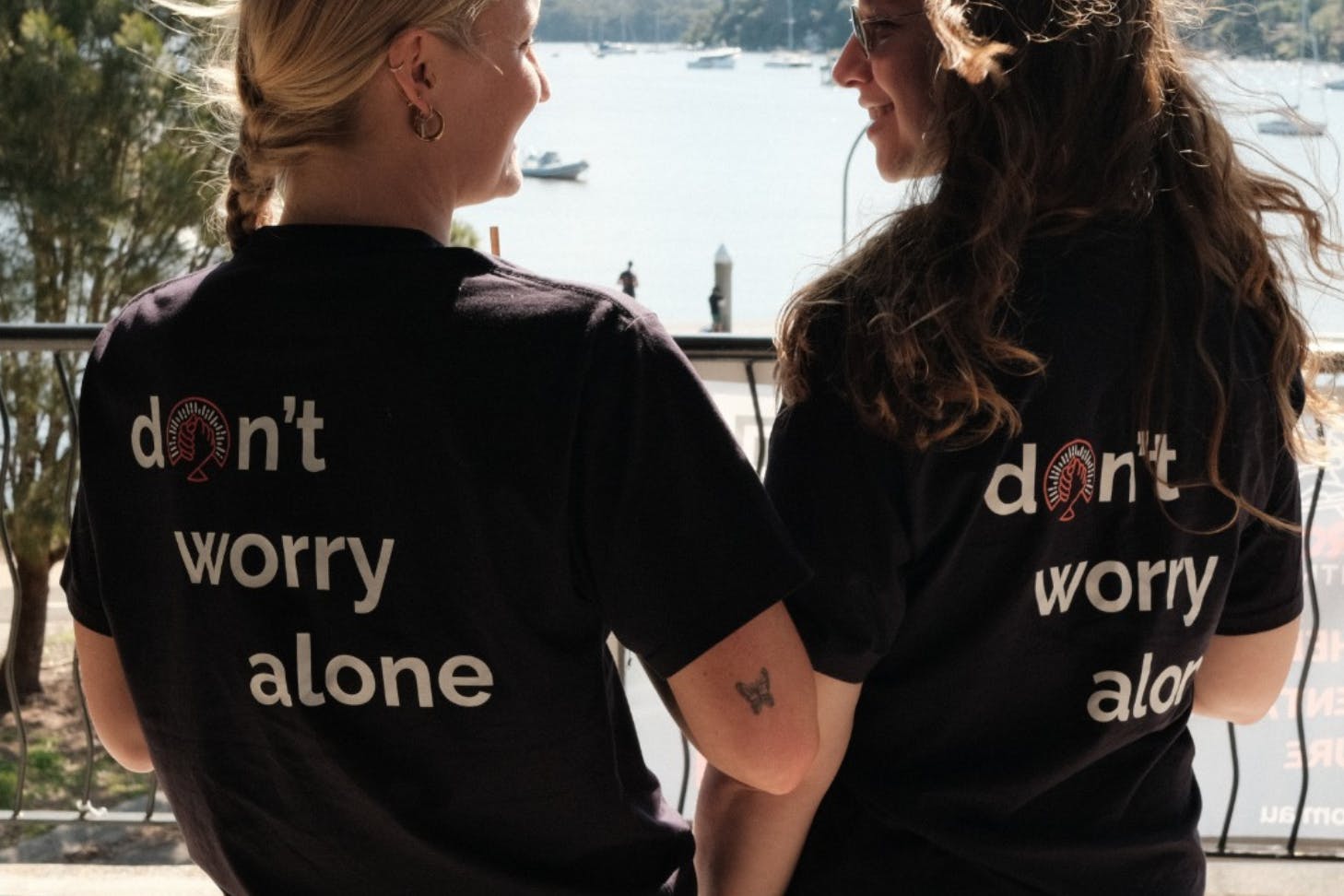 two girls face away from the camera with shirts that read 'don't worry alone'